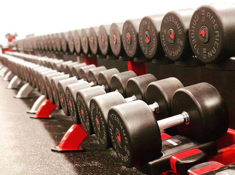 View of American Barbell Urethane Dumbbells at a gym on a red and back dumbbell rack